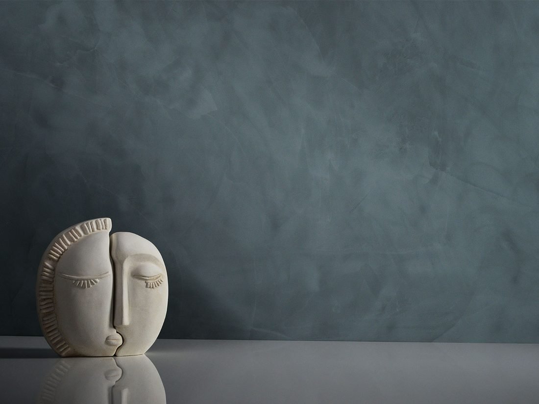 Dune Spatolato Marmorino Matt finish on a dark blue-grey wall, styled with a carved stone face sculpture